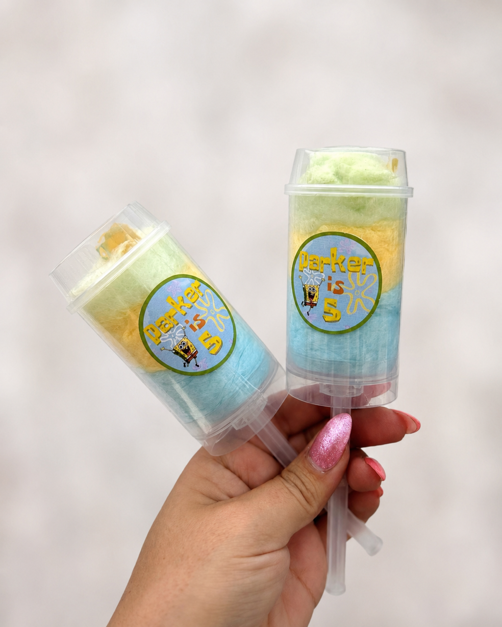 Hand holding colorful layered push-up cotton candy favors with custom SpongeBob-themed labels