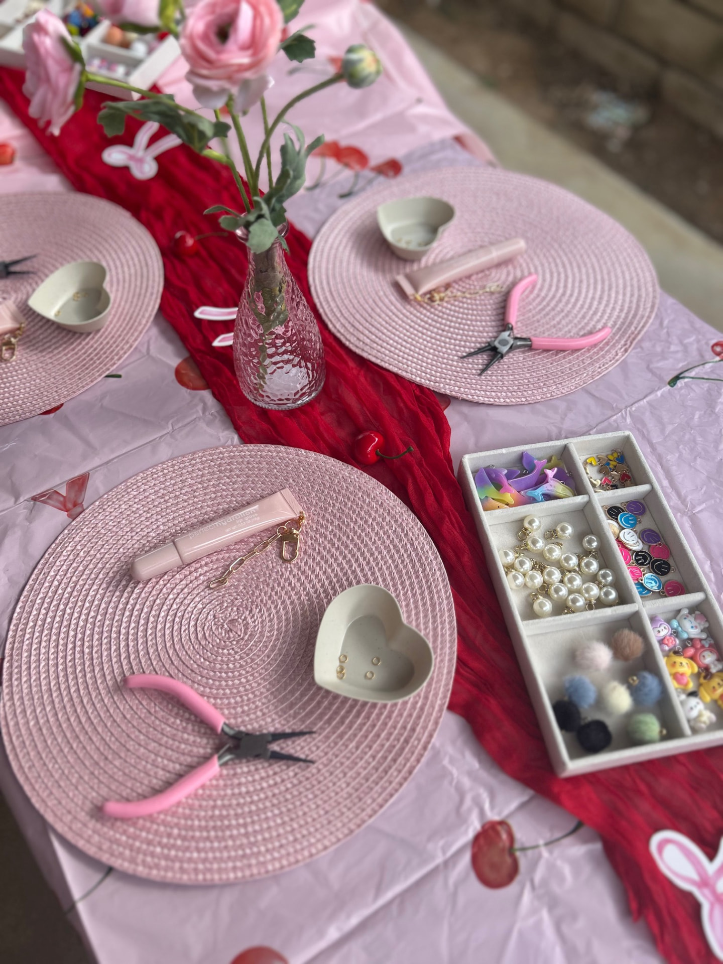 Styled lip gloss and charm keychain station with pink placemats, pearl beads, charms and gloss tubes
